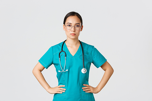 Covid-19, healthcare workers, pandemic concept. Confident determined asian female nurse helping patients, working with coronavirus disease, looking ready, wearing scrubs and glasses, white background.