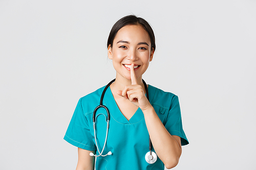 Healthcare workers, preventing virus, quarantine campaign concept. Smiling pretty asian doctor, nurse in scrubs smiling, shushing, asking stay quiet, standing white background.