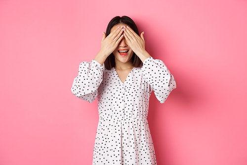 Happy romantic asian girl waiting for surprise, close eyes and smiling amazed, anticipating something, standing over pink background.