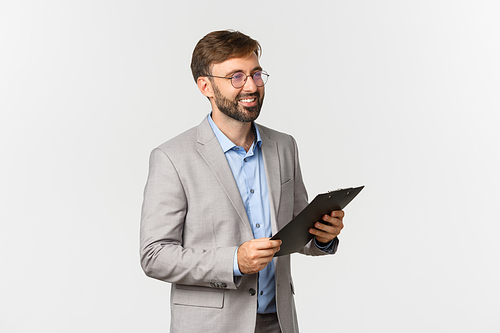 Profile shot of handsome confident businessman, wearing glasses and gray suit, holding clipboard and looking right, smiling while making presentation, white background.