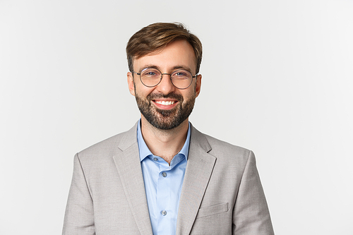 Close-up of confident bearded businessman in gray suit and glasses, smiling self-assured, standing over white background.