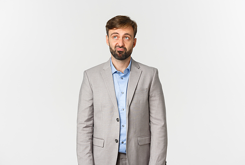 Portrait of skeptical and upset bearded male office worker in grey suit, looking disappointed at upper left corner logo, standing over white background.