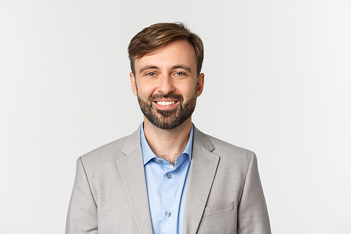 Close-up of confident bearded businessman in gray suit, smiling self-assured, standing over white background.