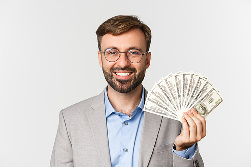 Close-up of male entrepreneur in gray suit and glasses smiling, showing money, standing over white background.