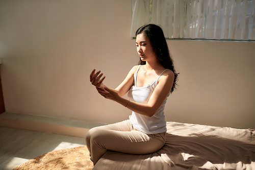 young woman applying moisturizer cream on her arm in her bedroom