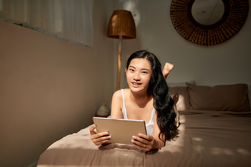 Happy  woman lying on the bed with tablet computer and looking at camera