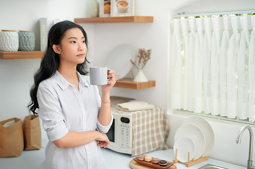Shot of smiling young woman drinking a cup of coffee in the kitchen at home.