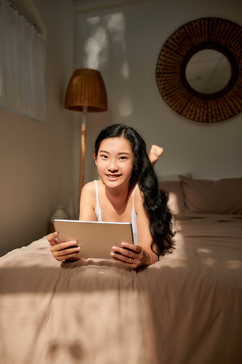 happy young asian pretty woman video call chat on digital mobile tablet on bed at home in morning