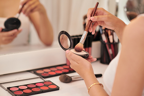 Beautiful young woman looking in the mirror and applying cosmetic with a big brush