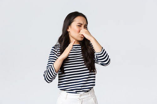 Lifestyle, beauty and fashion, people emotions concept. Disgusted korean girl shut nose and waving hand from disgust and aversion as sniff awful disgusting smell, standing white background.