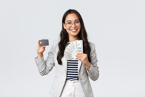 Business, finance and employment, entrepreneur and money concept. Successful asian businesswoman showing how increase income, hold credit card and money, smiling camera.