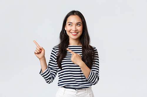 Lifestyle, people emotions concept. Excited good-looking asian girl smiling pleased as found excellent product, pointing fingers left at advertisement and looking satisfied, recommend promo.