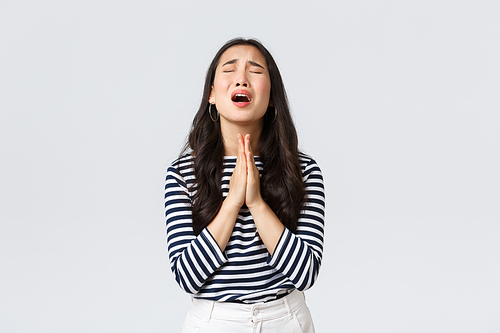 Lifestyle, people emotions and casual concept. Desperate hopeful asian girl making wish, close eyes and hold hands in pray, pleading god to have something, making wishful face, white background.