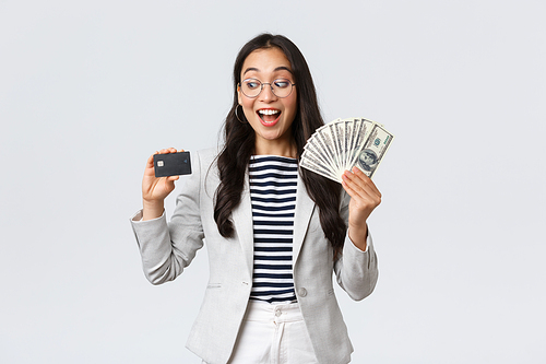 Business, finance and employment, entrepreneur and money concept. Indecisive cute asian office lady thinking about putting cash on deposit, looking excited at credit card, white background.