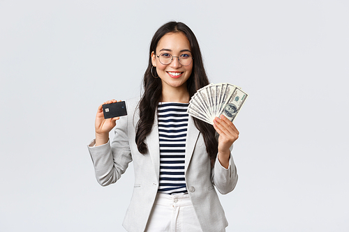 Business, finance and employment, entrepreneur and money concept. Successful asian businesswoman showing how increase income, hold credit card and money, smiling camera.