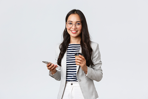 Business, finance and employment, female successful entrepreneurs concept. Professional asian businesswoman in glasses, having lunch, drinking takeaway coffee and using mobile phone.
