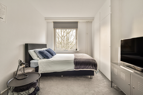 The interior of a bedroom with a gray and white design and a large window in a cozy apartment