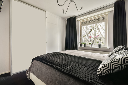 The interior of a bedroom with a black and gray design and a large window in a cozy apartment