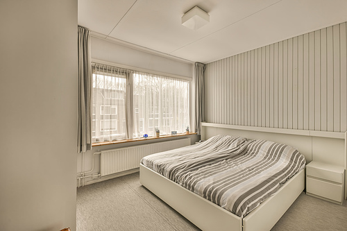 The interior of a small bedroom with a double bed on a carpet floor in a modern house