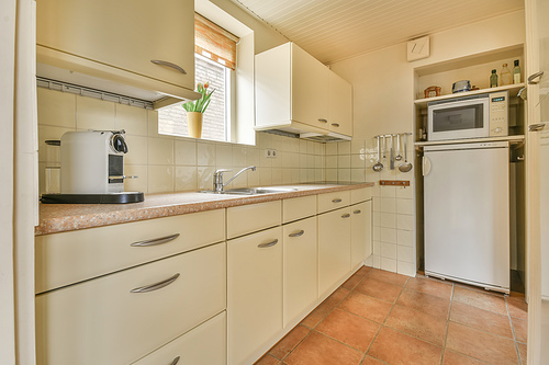 The interior of the kitchen with light furniture on the tiled floor in a cozy house