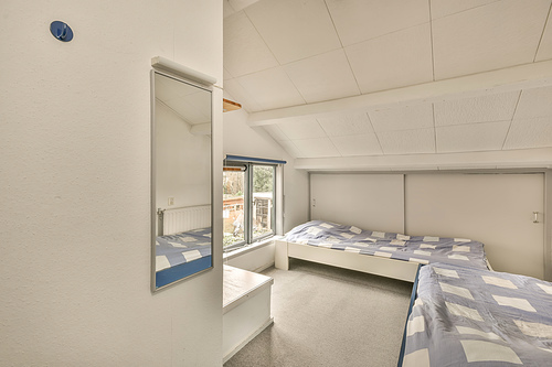 The interior of a small bedroom with a two beds on a carpet floor near to thw window in a modern house