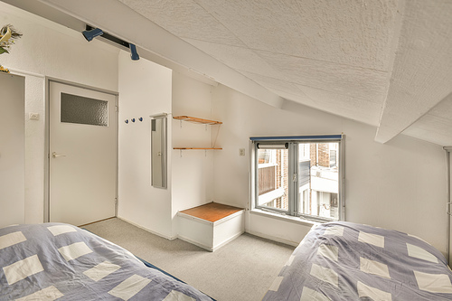 The interior of a small bedroom with a two beds on a carpet floor near to thw window in a modern house