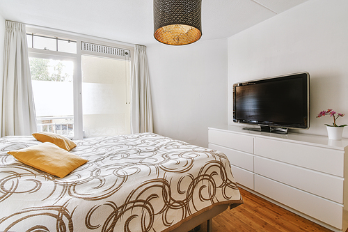 The interior of a bedroom with access to a balcony and a double bed on the parquet floor of a modern house