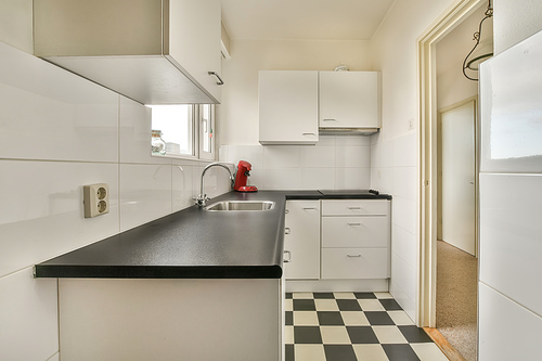 A small kitchen with lots of cabinets and a metal sink on the tiled floor