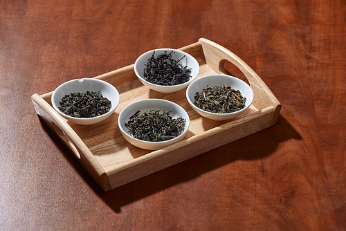 the white drinking bowls of assortment of dry tea in order on wooden background