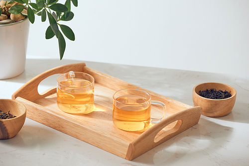 Hot tea is in the glass. Placed on a wooden tray.