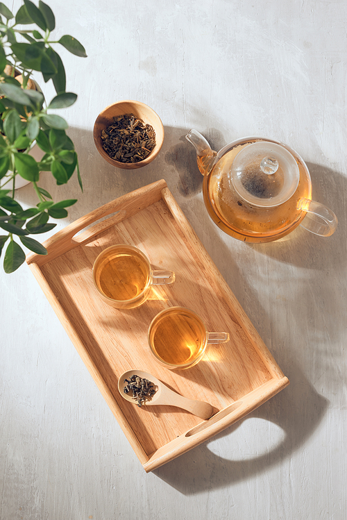 Hot tea is in the glass. Placed on a wooden tray.