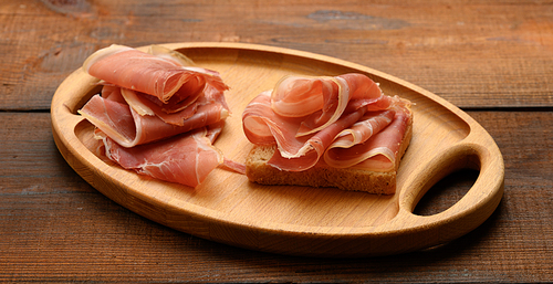 sandwich with a white square slice of bread and slices of prosciutto on a wood board