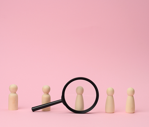 wooden figures of men stand on a pink background and a black magnifying glass. Recruitment concept, search for talented and capable employees, career growth