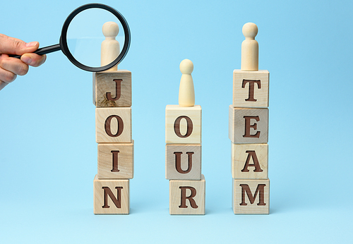 wooden figurines of men stand on cubes with the inscription and a hand with a magnifying glass on a blue background. Recruitment concept, search for talented and capable employees, career growth