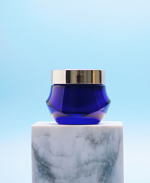 Facial cream jar on blue background, luxury skincare products, beauty and cosmetics.
