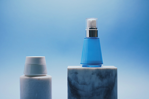 Serum bottle and facial cream jar on blue background, luxury skincare products, beauty and cosmetics.