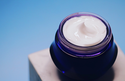 Anti-aging skincare and cosmetics, beauty face cream in jar on blue background.