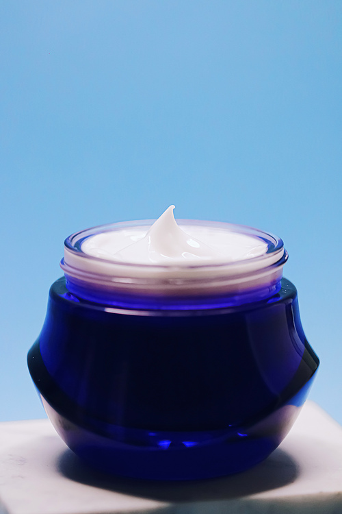 Anti-aging skincare and cosmetics, beauty face cream in jar on blue background.