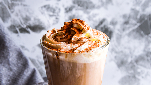 Hot latte macchiato coffee with caramel on tabletop outdoors. Natural hard daylight. Soft focus Close up view