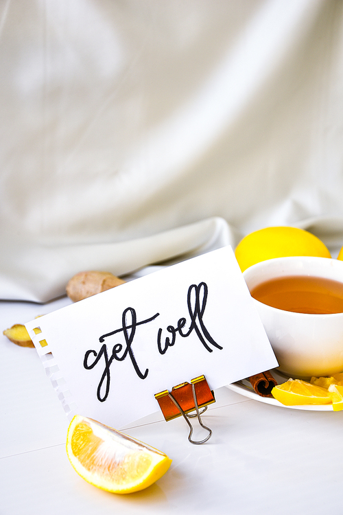 GET WELL - written on piece of paper among the products for the treatment of common cold - lemon, ginger, chamomile tea. Vitamin natural drink. Cinnamon anise star.