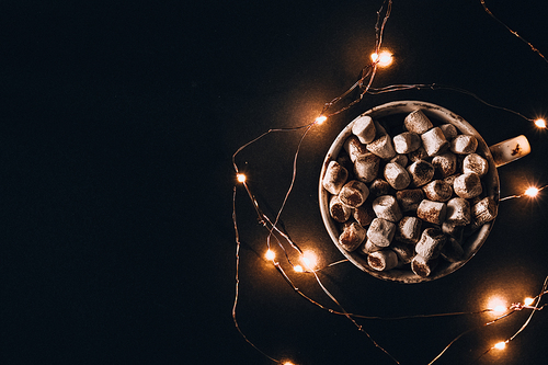 Cup with hot winter cacao and marshmallows at night. Christmas garland lights. Good night sweet dreams. Cozy winter days. Hygge.