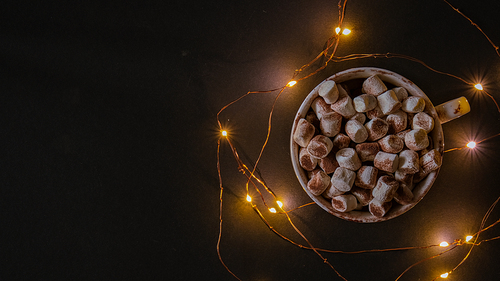 Cup with hot winter cacao and marshmallows at night. Christmas garland lights. Good night sweet dreams. Cozy winter days. Hygge.