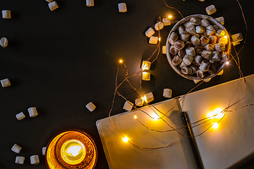 Cup with hot winter cacao and marshmallows at night. Christmas lights. Tea light candles. Empty notebook with pen Good night sweet dreams. Cozy winter days. Hygge.