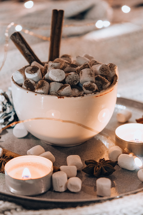 Cup with hot winter cacao and marshmallows cinnamon sticks on bed. Christmas lights. Pine cones decoration. Cozy winter days. Hygge. Tea light candles
