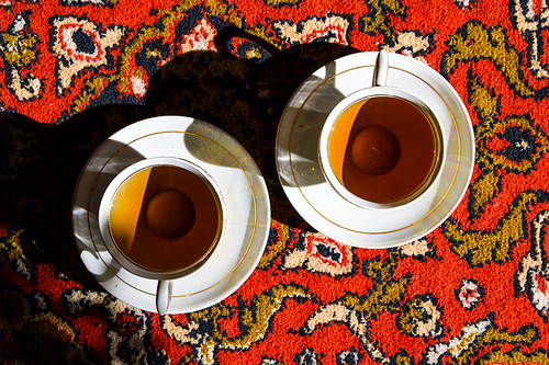 Two vintage porcelain cups of coffee or tea on the oriental turkish or asian carpet, tea ceremony, sunlight and deep shadow