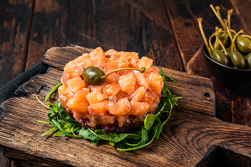Salmon tartare or tartar with red onion, avocado, arugula and capers. Dark wooden background. Top View.