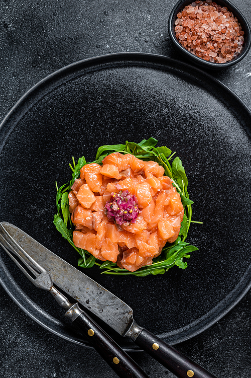 Raw Salmon tartare or tartar with red onion, arugula and capers in black plate. Black background. Top View.
