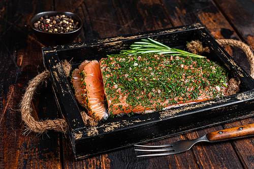 Salmon Gravlax cured with dill and salt in wooden tray. Dark wooden background. Top view.