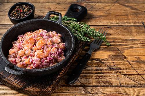 Tartar or tartare with salmon fish, red onion, arugula and capers in a pan. Wooden background. Top View. Copy space.