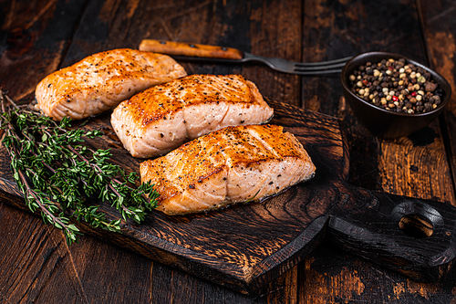 Fried Salmon Fillet Steaks on a wooden board with thyme. Dark wooden background. Top view.